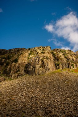 Snowdonia, Galler 2025.09.21 Dağlık bir uçurum Dağılmış kayalar ve parlak mavi gökyüzü altında güneşli dokular. 