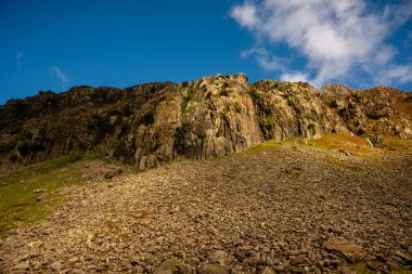 Snowdonia, Galler 2025.09.20 Sunlit kayalık yamaçları Eryri Ulusal Parkı 'nın engebeli dağlık arazisinde derin mavi bir gökyüzü altında dramatik uçurumların altında.. 