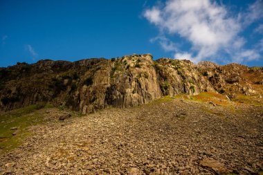 Snowdonia, Galler 2025.09.20 Sunlit kayalık yamaçları Eryri Ulusal Parkı 'nın engebeli dağlık arazisinde derin mavi bir gökyüzü altında dramatik uçurumların altında.. 