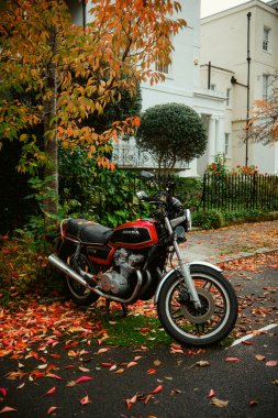 Chiswick, Londra, İngiltere 2025.10.22 Klasik Honda motosikleti sonbahar ağaçları ve renkli yapraklarla çevrili yapraklı bir caddede park halinde.. 