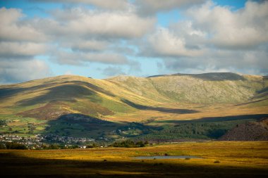 Snowdonia, Galler 2025.09.21 Sıcak güneş ışığı ve derin gölgeler kayan tepeler ve kayan bulutların altında küçük bir vadi köyü boyunca uzanır.. 
