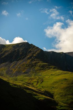 Snowdonia Ulusal Parkı, Galler 2025.09.21 Mavi gökyüzünün altında sıcak güneş ışığıyla aydınlatılan engebeli bir dağ yamacı ve sürüklenen bulutlar Galler dağlarının saf güzelliğini yansıtıyor.. 