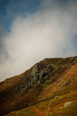 Snowdonia, Galler 2025.09.21 Sonbahar renkleriyle kaplı engebeli dağ yamacı dramatik bulutlu gökyüzünün altında kayalık bir sırt var.. 