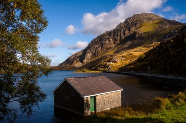Snowdonia, Galler 2025.09.21 Yeşil kapılı taş kayıkhane Llyn Ogwen 'in kenarında güneşli Tryfan dağının altında, mavi gökyüzünün altında.. 