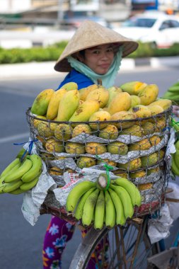 Typical street fruit vendor with palm-leaf conical hat moving at the street in road.