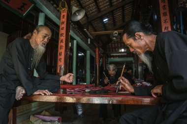 the old man with traditional black costume, white beard drawing calligraphy ancient distich in Long Son, Ba Ria Vung Tau,Vietnam to celebrating lunar new year coming. clipart
