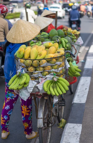 Typical street fruit vendor with palm-leaf conical hat moving at the street in road.