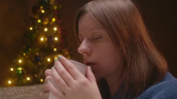Жінка в своїй квартирі п'є гарячий шоколад або глінтвейн з ялинкою на фоні. Реклама для гарячих напоїв . — стокове відео