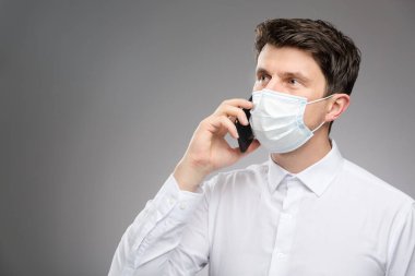 Yüz maskeli bir adam müşterisiyle telefonla konuşuyor. Koronavirüs salgınında koruyucu yüz maskesi takan bir ofis çalışanı.. 