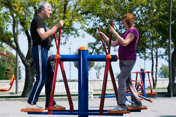 Pareja mayor haciendo ejercicios deportivos en el campo de deportes. Hombre y mujer jubilados haciendo entrenamientos cardiovasculares. — Foto de Stock