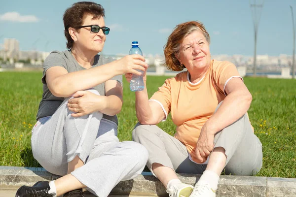 Deux pensionnées qui se reposent après s'être entraînées au parc. Concept de mode de vie sain. — Photo