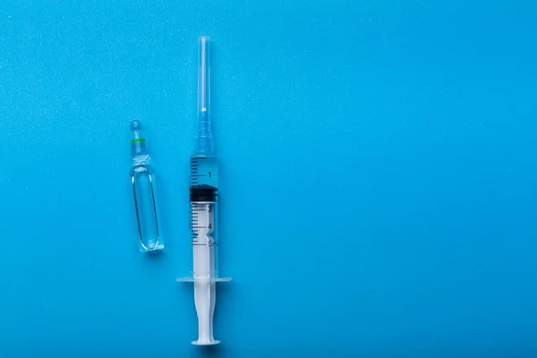 Coronavirus 'un pandemik zamanındaki aşıların sembolü olarak mavi arka planda enjeksiyonu olan bir şırınga.. — Stok fotoğraf