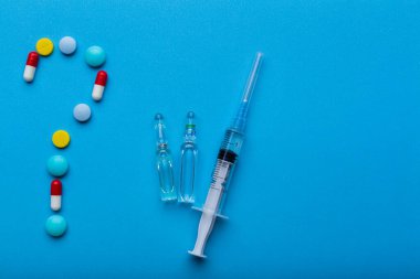 Aşı yapmak ya da yapmamak için mavi zemin üzerinde haplardan yapılmış soru işareti olan bir şırınga, reçete için alanı kopyala.