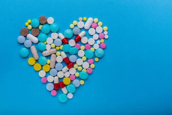 Un montón de pastillas en forma de corazón sobre un fondo azul como símbolo de tratamiento para proteger el corazón. Fotos de stock