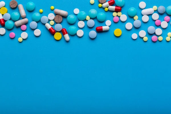 A lot of multi-colored pills on blue background with free space for text, as a concept of medical treatment with a prescription.
