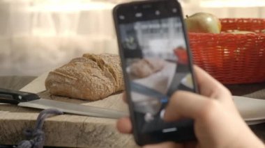 Cep telefonuyla ev yapımı ekmeğin fotoğrafını çeken bir adam kurstan kalma internet tarifiyle evde yemek pişiriyor..