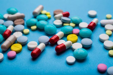 Bir sürü renkli hap ve kapsül mavi arka planda ilaç bağımlılığı konsepti olarak.. 
