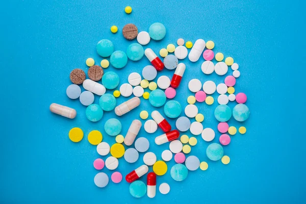 Um monte de comprimidos multicoloridos e cápsulas em um fundo azul como um conceito de dependência da medicina. — Fotografia de Stock