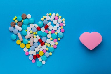 Sağlıklı bir kalbin tedavi sembolü olarak kalp şeklinde mavi arka planda bir sürü hap..