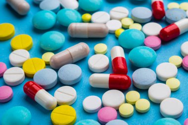 Bir sürü renkli hap ve kapsül mavi arka planda ilaç bağımlılığı konsepti olarak.. 