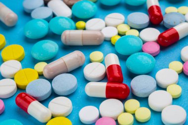 Bir sürü renkli hap ve kapsül mavi arka planda ilaç bağımlılığı konsepti olarak.. 