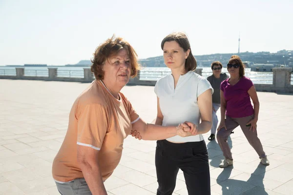 Mujer joven entrenador ayuda a la mujer mayor haciendo ejercicios de estiramiento. — Foto de Stock