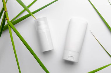 Beyaz arka planda yeşil yapraklı yüz ve vücut kremi olan beyaz tüpler. Yaz için özel yüz bakımı.