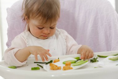 Bebek sebze yer, masaya pisler, kollarıyla yer ve sütten kesilir. Yüksek kalite fotoğraf