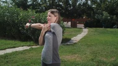 Parkta esneme egzersizleri yapan kadın, sağlıklı yaşam tarzı, vücut bakımı ve eğlence etkinliği teması. Kişisel antrenör dersten önce esneme hareketleri yapıyor.