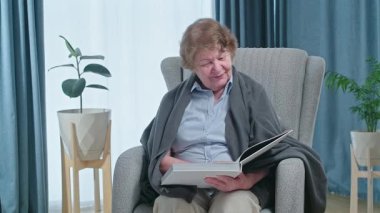 Senior woman reading book sitting in armchair. Home leisure activity after retirement . High quality 4k footage