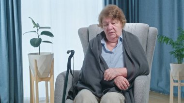 Mature woman in armchair feeling unhealthy and coughing, flu symptoms and treatment concept. High quality 4k footage