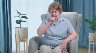 Mature woman in armchair feeling unhealthy and coughing, flu symptoms and treatment concept. High quality 4k footage
