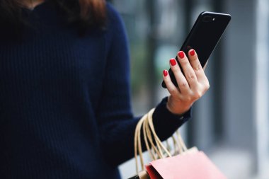 Kadın cep telefonuyla alışveriş yapıyor.