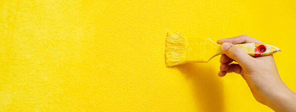The painter is painting the walls in yellow with the interior of the home living room.