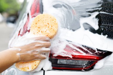 İnsanlar elleri sarı sünger ve köpük temizleyici ile araba yıkamak için el ele tutuşuyorlar. Konsept araba yıkama. İleti yazmak için yer bırakın. 