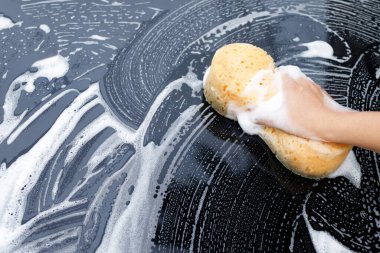 İnsanlar elleri sarı sünger ve köpük temizleyici ile araba yıkamak için el ele tutuşuyorlar. Konsept araba yıkama. İleti yazmak için yer bırakın. 