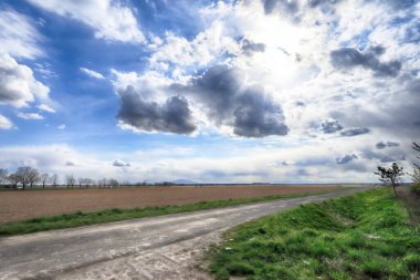 Fırtınalı bir nisanın son günlerinde tarlaların arasında boş, yerel bir yol. Güzel bulutlu bahar manzarası.