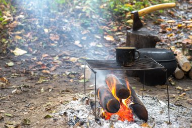 Izgaranın üzerindeki metal, siyah, ıslak kupa. Açık bir ateşte. Yürüyüş takımlarının ve sonbahar yapraklarının arka planında..
