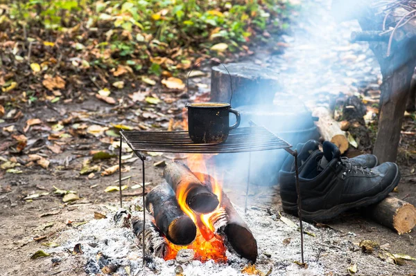 Metalowy czarny kubek sadzy na grillu na otwartym ogniu na tle sprzętu turystycznego i jesiennych liści. — Zdjęcie stockowe