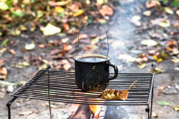 Metallschwarzer rußiger Becher auf dem Grill am offenen Feuer vor dem Hintergrund von Herbstblättern. Hintergrund. — Stockfoto