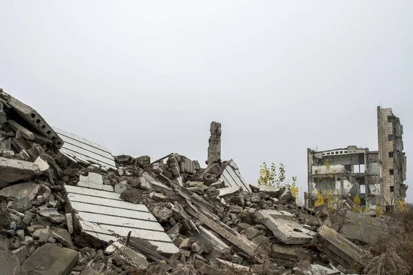 Bulanık sisli, tarafsız gri gökyüzüne karşı beton gri enkaz yığını olan harabe bir bina. Arkaplan