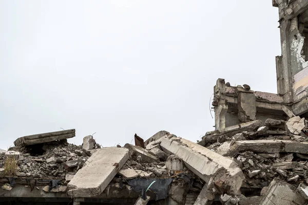 A ruined building with a pile of concrete gray debris against a neutral gray sky in a hazy haze. Background — Stock Photo, Image