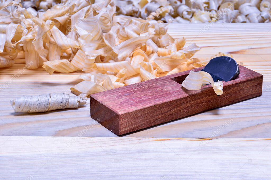 Japanese wooden plane made of red oak with a pile of shavings on a smooth wooden surface. Background.