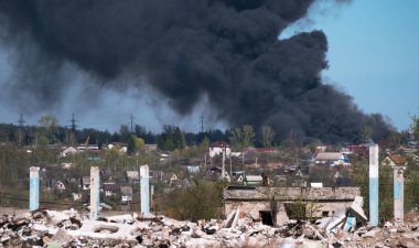 Harabe bir binanın beton kalıntıları. Mavi bir gökyüzüne karşı siyah dumanların arka planında çıkıntılar var. Arkaplan