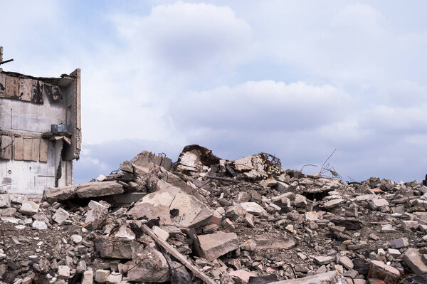 A pile of concrete wreckages of construction debris against the background of the remains of the building and the gray sky with clouds. Background.
