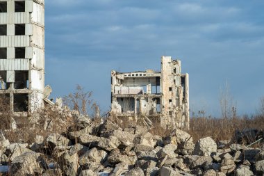 Önünde beton moloz yığını olan gri bulutlu mavi gökyüzüne karşı yıkılmış bir bina. Geçmişi. Önplana seçmeli odak.