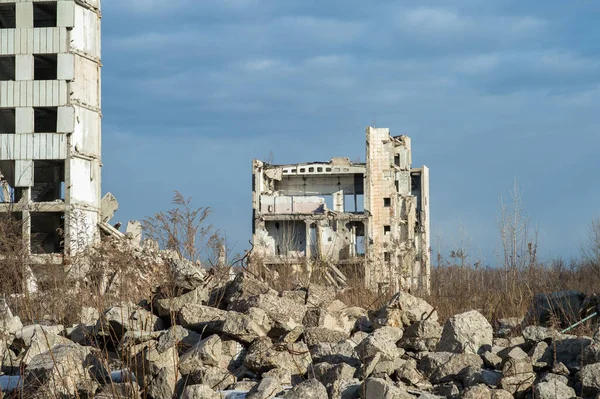 Önünde beton moloz yığını olan gri bulutlu mavi gökyüzüne karşı yıkılmış bir bina. Geçmişi. Önplana seçmeli odak.