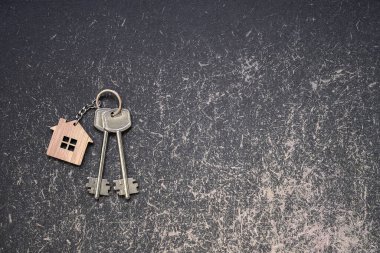 Ahşap ev anahtarlığı olan anahtarlar. Çizim tahtasının karanlık, pejmürde arka planına yakın plan. Arkaplan.