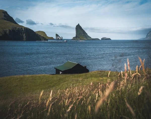 Небольшой деревенский дом перед воротами Дрангарнир и остров Тиндхольмур и Майкинес на заднем плане, Фарерские острова. — стоковое фото