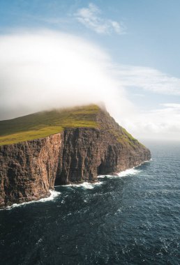 Faroe Adaları Traelanipa. Kölelerin kaya uçurumu okyanusun üzerinde Sorvagsvatn Gölü 'nün yanında yükseliyor. Faroe Adaları 'ndaki vajina adasında bulutlar ve mavi gökyüzü..